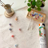 Paint by numbers kit with paint bottles, brushes, and a plant on a table.
