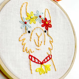 Embroidery hoop with a llama design using yellow, red, and blue thread on white fabric.