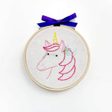 Embroidery hoop with unicorn design and blue ribbon on a white background