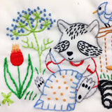Embroidered design of a raccoon with flowers and a bird on a white background