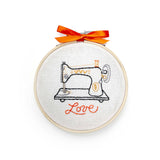 Embroidery hoop with a sewing machine design and 'love' text on a white background