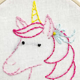Embroidery of a unicorn with pink mane and yellow horn on white fabric.
