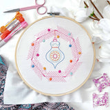 Embroidery hoop with colorful thread design on a white fabric background with embroidery supplies.