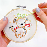 Embroidery hoop with a fox design being worked on, held by hands with light purple nail polish.