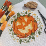 Cross-stitched pumpkin design on fabric with embroidery threads and scissors.