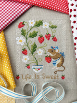Cross-stitched design with strawberries, a mouse, and 'Life is Sweet' text on fabric.