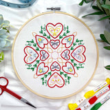 Embroidery hoop with heart and butterfly design on white fabric, surrounded by embroidery supplies.