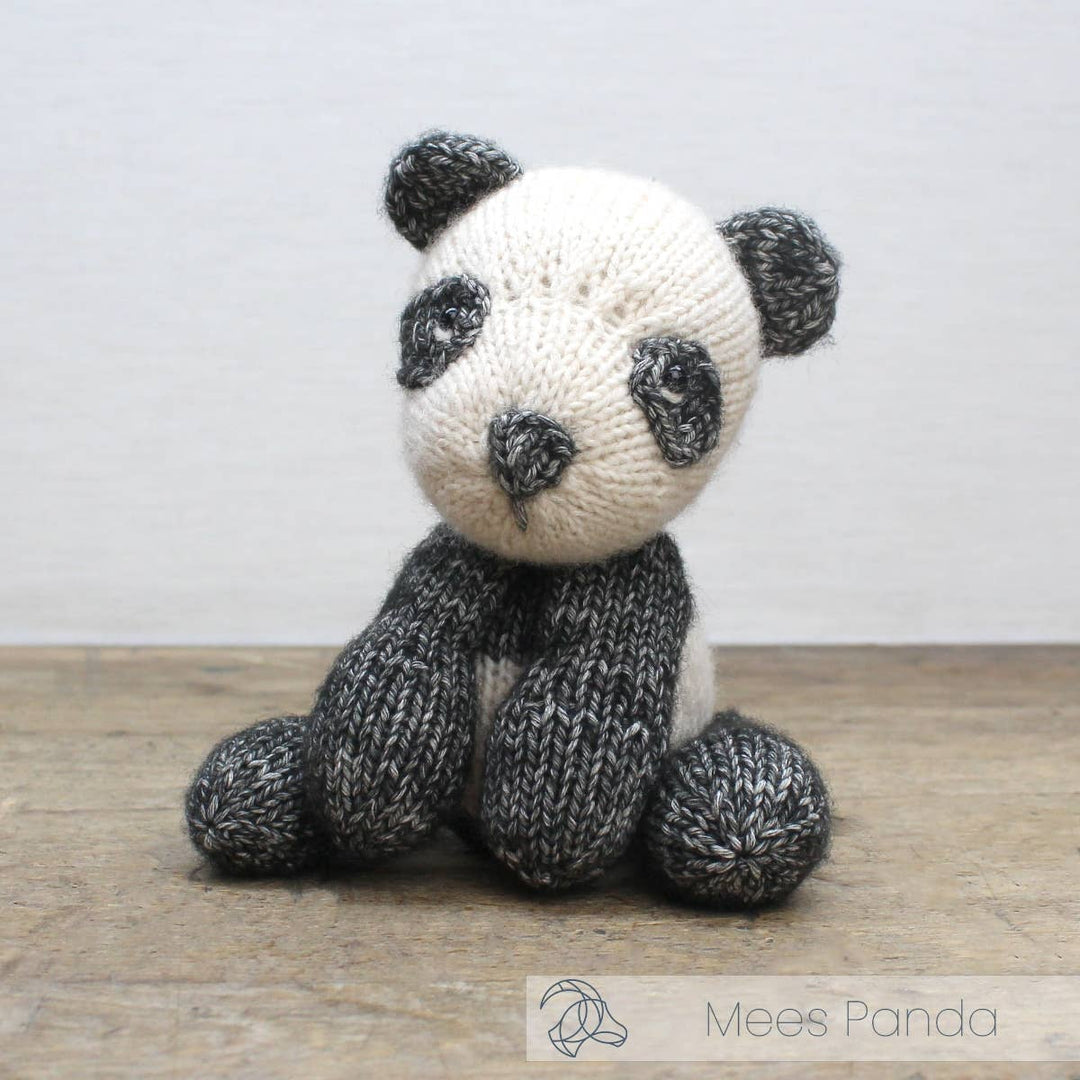Knitted panda toy on a wooden surface with a plain background