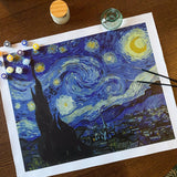 Painting of 'Starry Night' by Van Gogh with paint supplies on a wooden table.