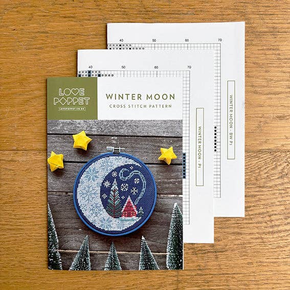 Cross stitch kit with pattern paper, tools, and decorative elements on a wooden surface