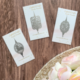 Three 'Eight22Crafts' needle threader cards on a wooden surface with flowers.