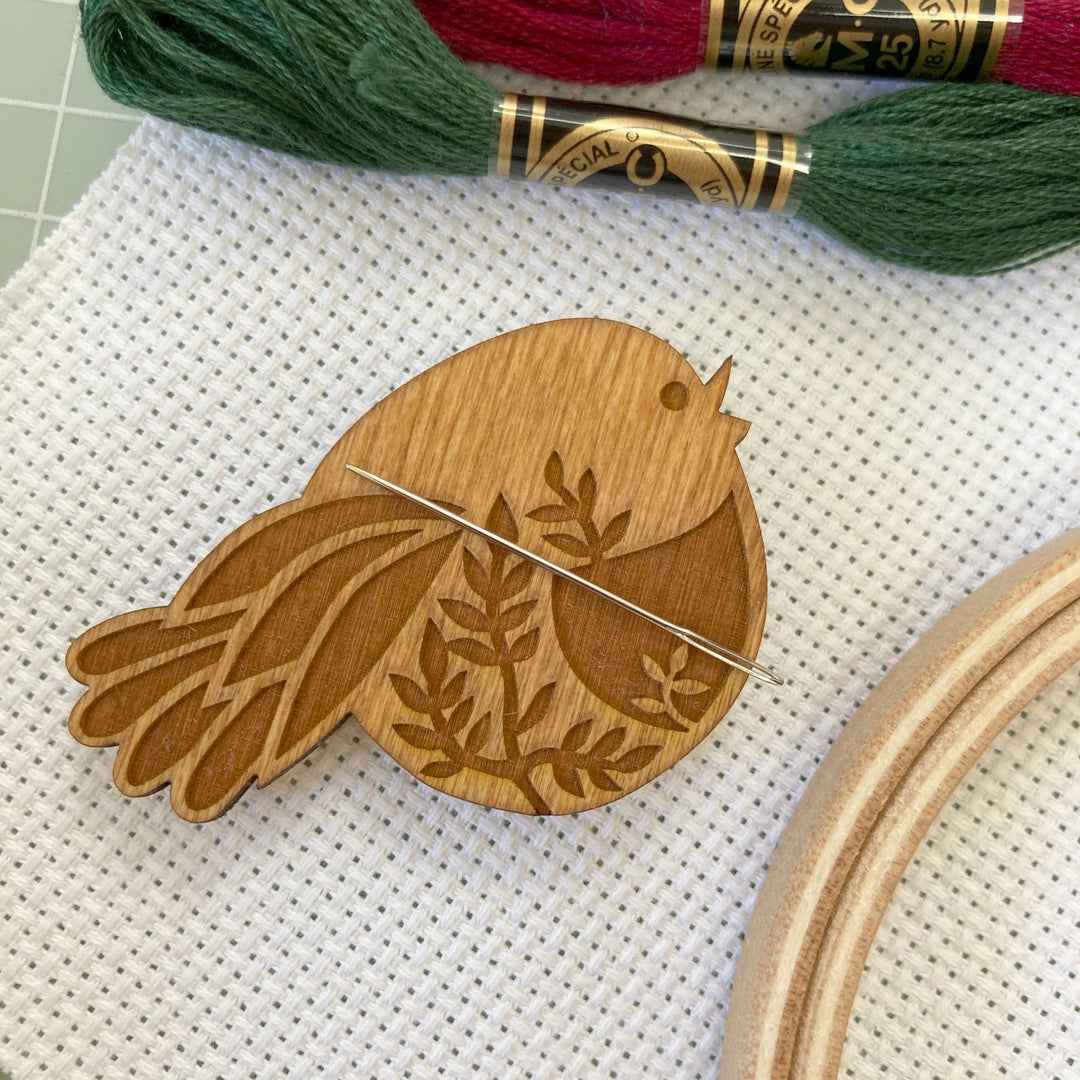 Wooden bird-shaped pin on a cross-stitch fabric with embroidery floss and hoop in the background.