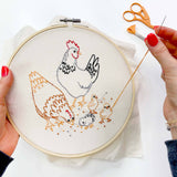 Embroidery hoop with chicken design and embroidery tools on a white background