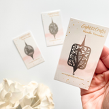 Hand holding a card with a needle threader design, surrounded by white flowers on a light background