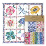 Colorful quilt with floral and nature-themed blocks and a kit packaging on a white background