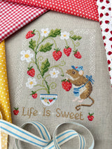 Cross-stitched design with a mouse, strawberries, and flowers on fabric.