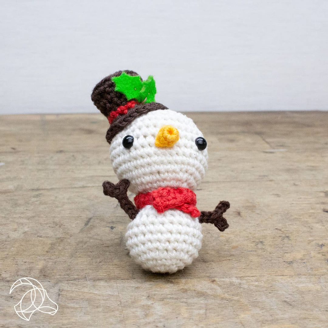 Crocheted snowman toy with a top hat, scarf, and carrot nose on a wooden surface.