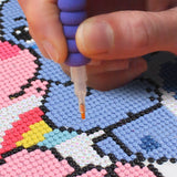 Hand using a bead placer to create a colorful bead pattern on a surface.