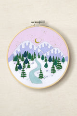 Embroidery hoop with a winter landscape design featuring trees, mountains, and a river.