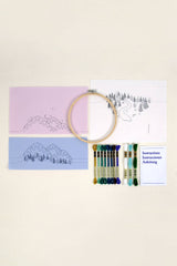 Embroidery hoop with colorful threads, patterned paper, and instructions on a beige background