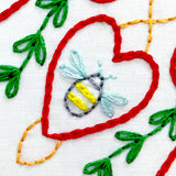 Embroidery design with a bee and heart shape on fabric.