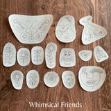 Set of white embroidered patterns on a wooden surface with 'Whimsical Friends' text.