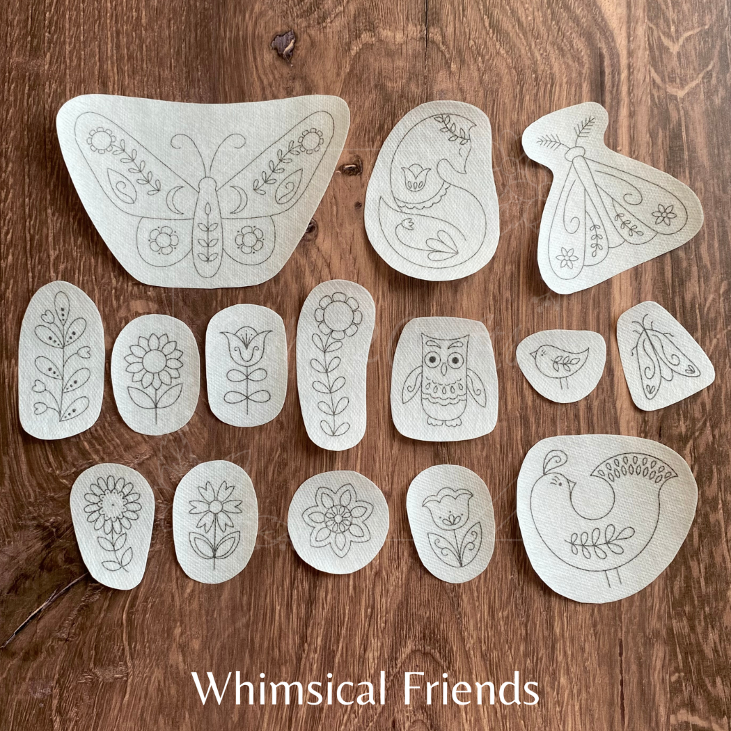 Set of white embroidered shapes with various designs on a wooden surface, labeled 'Whimsical Friends'.