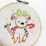 Embroidery hoop with a white dog wearing a red scarf and green antlers on a white background
