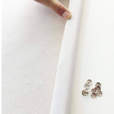 Close-up of a hand holding white fabric with metal buttons on a light background
