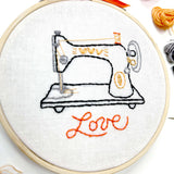 Embroidery hoop with a sewing machine design and 'love' text on white fabric.