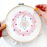 Embroidery hoop with a colorful design being worked on, held by hands with yellow nail polish.