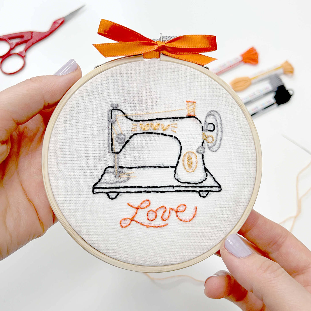 Embroidery hoop with a sewing machine design and 'love' text, held by a person.