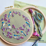 Embroidery hoop with bird and floral pattern on green fabric, with embroidery threads and tools.