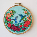 Embroidery hoop with colorful floral and hummingbird design on a light blue background
