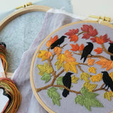 Embroidery hoop with autumn-themed design featuring leaves and birds.
