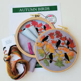 Embroidery hoops with autumn-themed designs and supplies on a white background