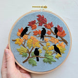 Embroidery hoop with autumn-themed design featuring birds and leaves.