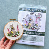 Embroidery hoop with completed bunny design and embroidery kit packaging on a blue background
