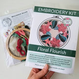 Embroidery kit with floral design, including a hand holding the kit and an embroidery hoop with thread.