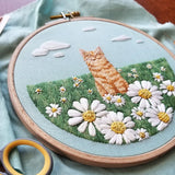 Embroidery hoop with a cat and floral design on a light blue fabric background