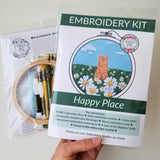 Embroidery kit with a cat and flowers design, held by a hand.
