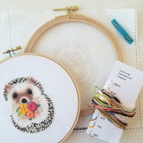 Embroidery hoop with a completed hedgehog design and embroidery kit on a white background