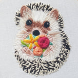 Embroidered patch of a hedgehog with flowers on a light gray background