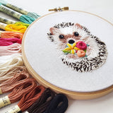 Embroidery hoop with a hedgehog holding flowers surrounded by colorful embroidery threads.