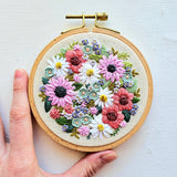 Embroidery hoop with floral design held by a hand on a light background