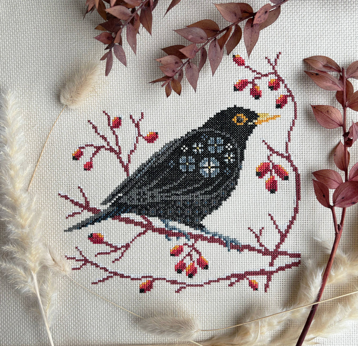 Cross-stitched bird on a branch with berries and leaves on fabric