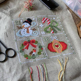 Cross-stitched snowman design on fabric with embroidery tools nearby