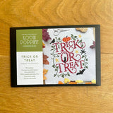 Cross stitch kit packaging with 'Trick or Treat' design on a wooden surface
