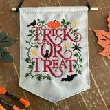 Embroidered banner with 'Trick or Treat' text on a wooden surface with Halloween decorations.