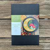 Cross stitch kit packaging with 'Woodland Moon' design on a wooden surface
